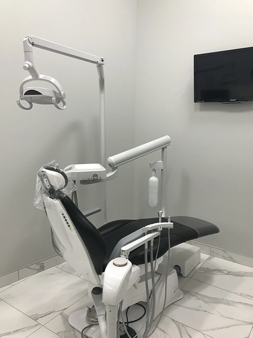 Dental chair with attached light and instruments in a modern, white-walled room.