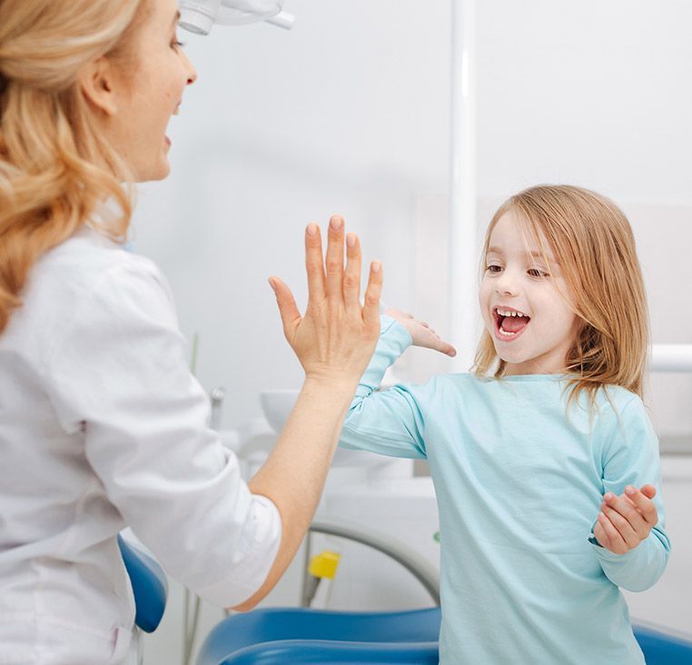 Dentist gives a high-five to a child in a dental office. Both are smiling.