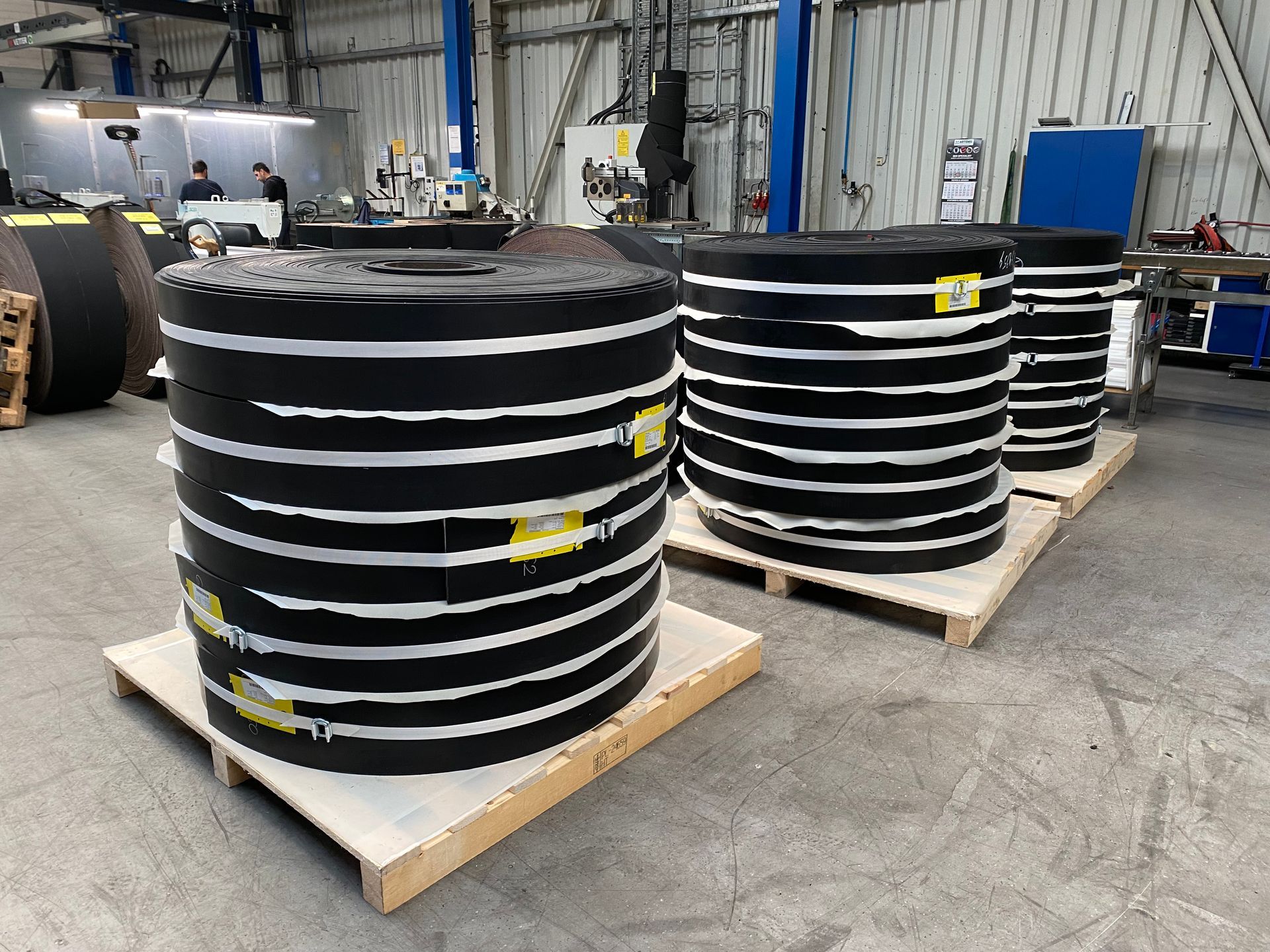 A large snow groomer with wide tracks and snow plowing blades, parked on a snowy mountain slope, surrounded by trees.