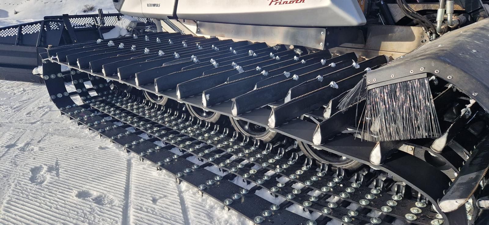 Snow groomers working together at night, clearing snow on a ski slope, with heavy snowfall and snow-covered trees.