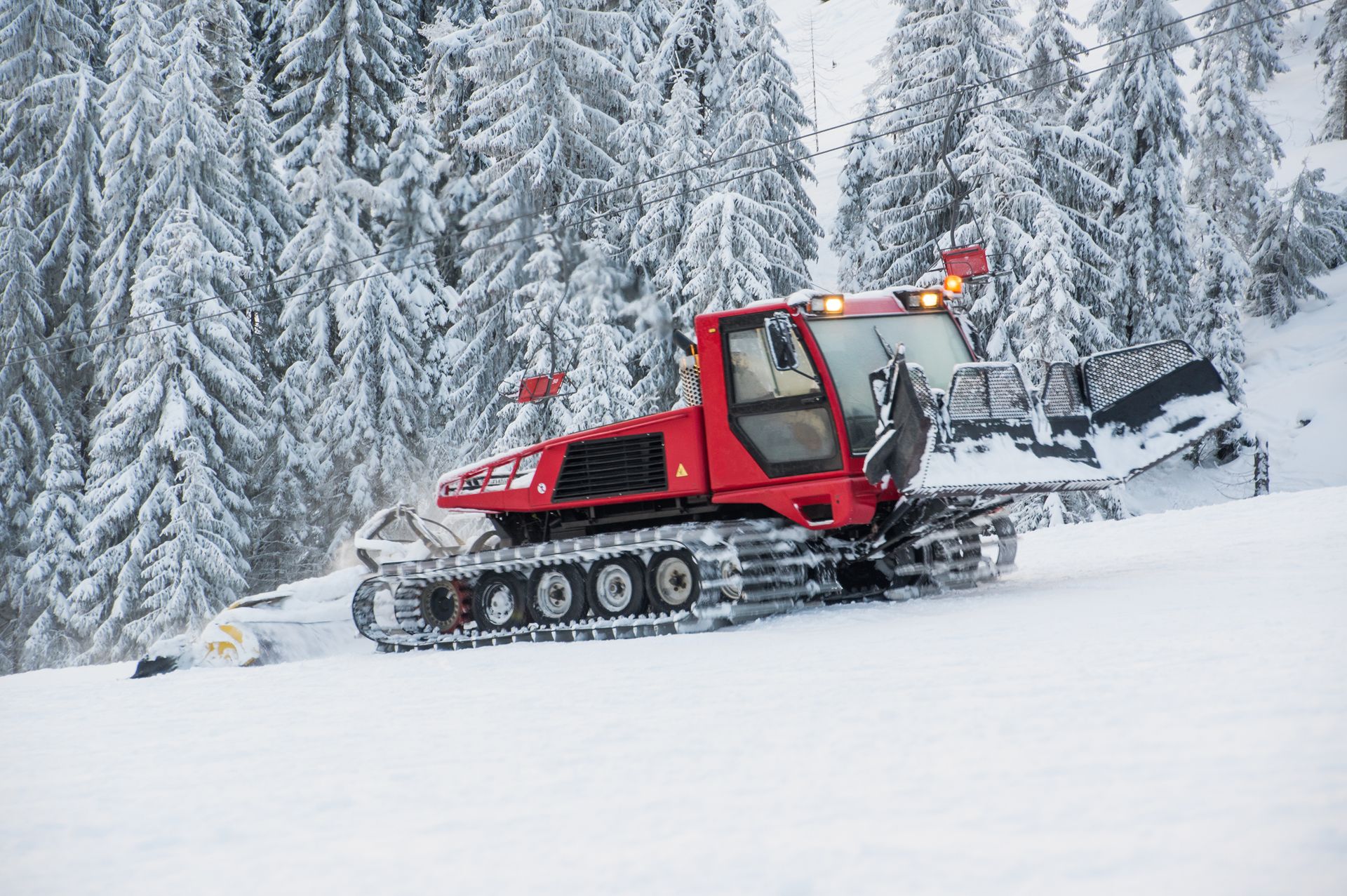 A red snow plow is driving down a snow covered slope.