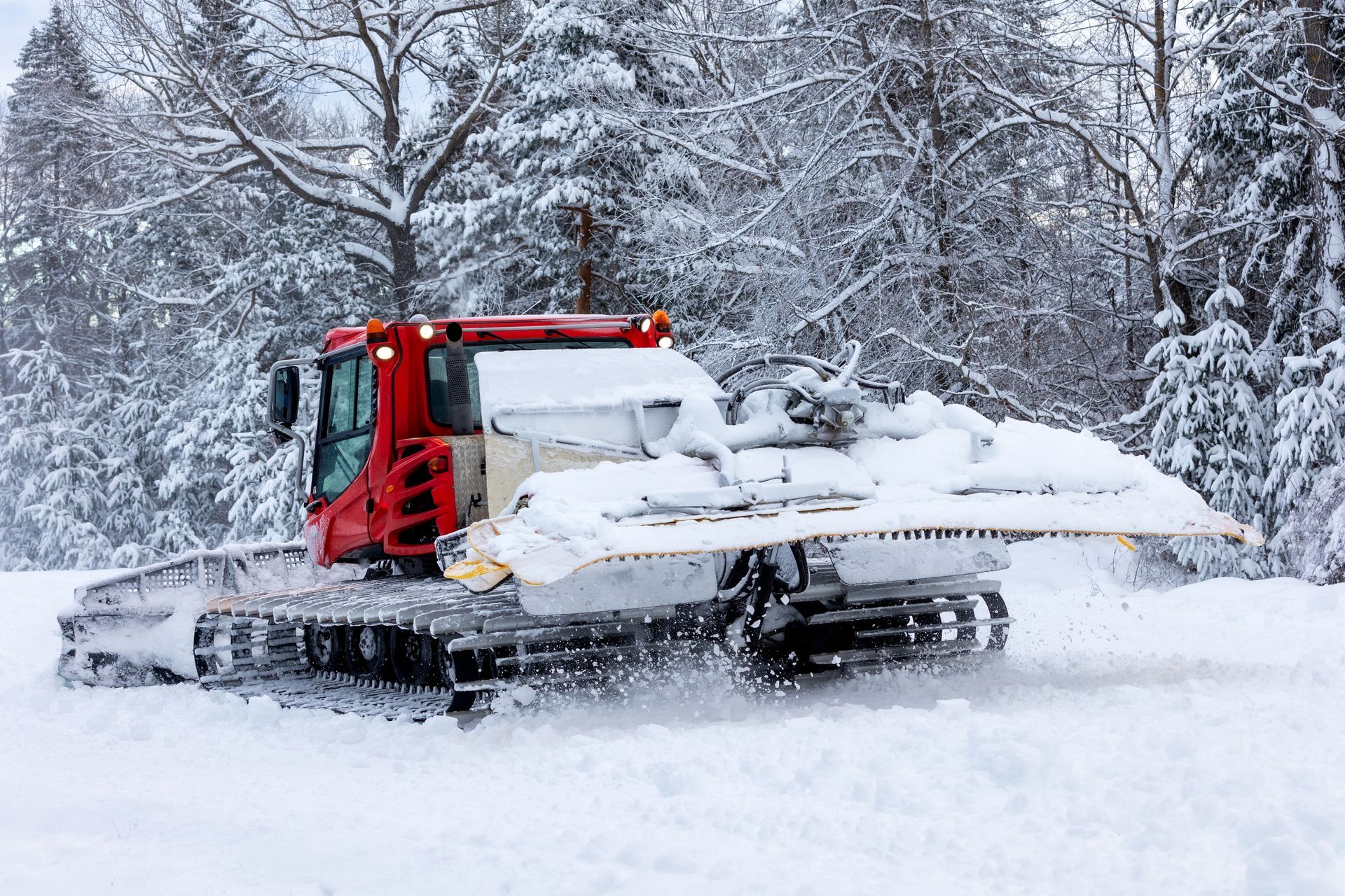 A snow plow is driving through a snowy forest.