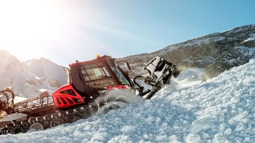 Snow groomers working together at night, clearing snow on a ski slope, with heavy snowfall and snow-covered trees.