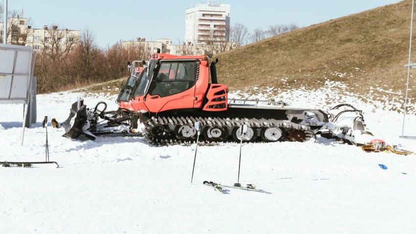 Snow groomers working together at night, clearing snow on a ski slope, with heavy snowfall and snow-covered trees.