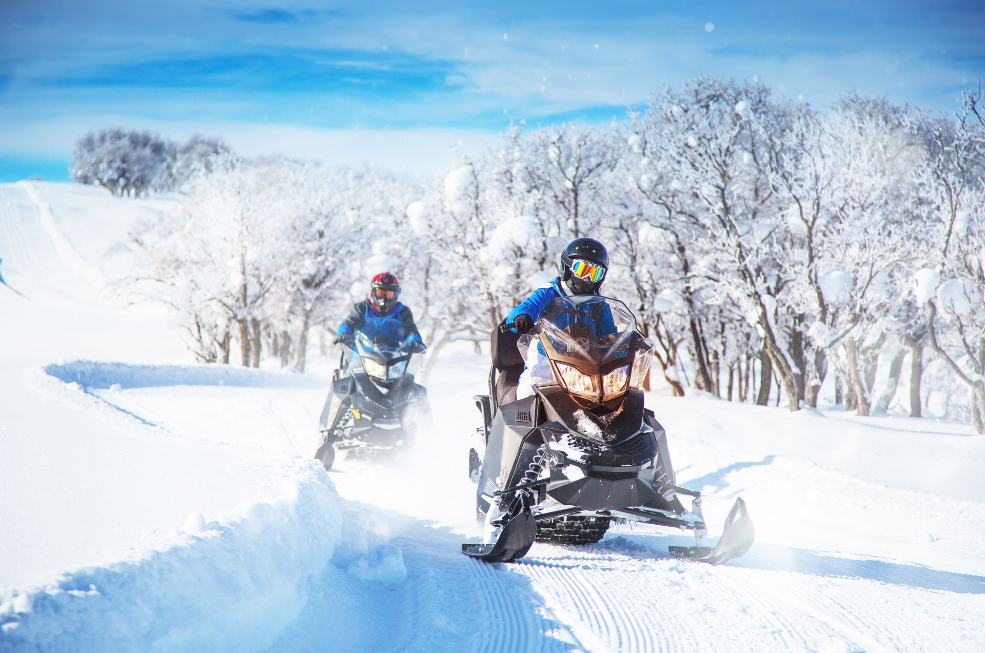 Two people are riding snowmobiles in the snow.