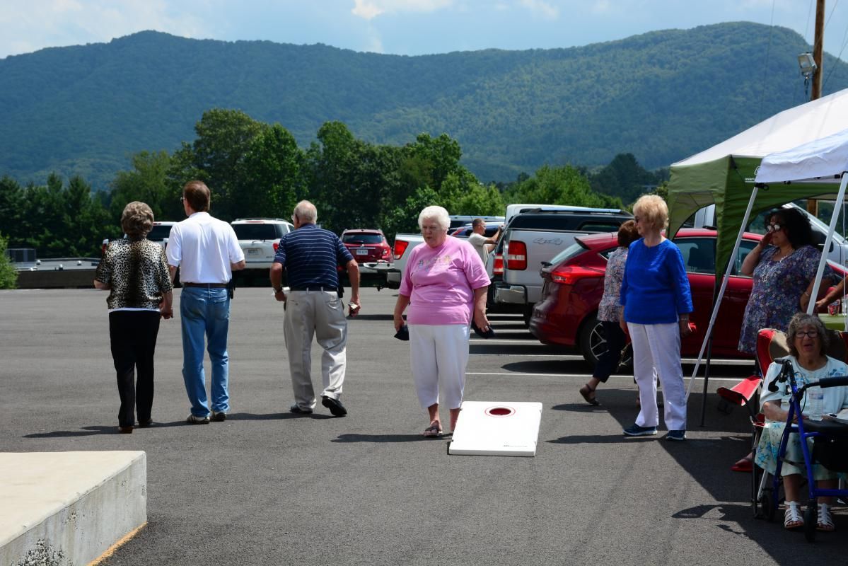 People playing cornhole outdoors, mountain backdrop.