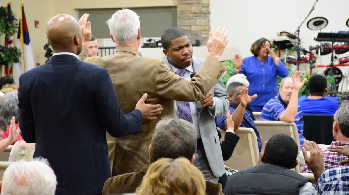 People with hands raised in church, one man being embraced by others.