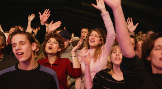 People singing with arms raised in an indoor gathering.