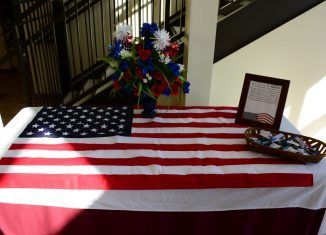 American flag draped table with flowers, framed document, and small basket.
