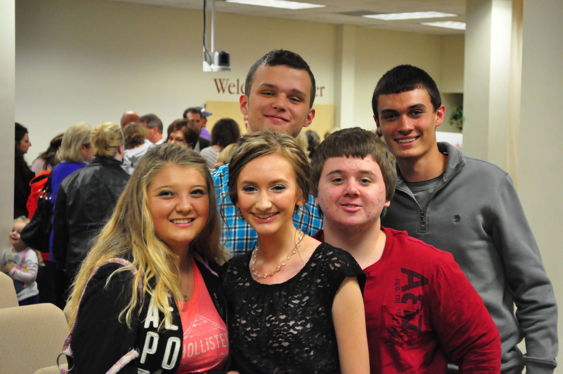 Group of five smiling young adults posing for a photo, indoors near a “Welcome Center” sign.