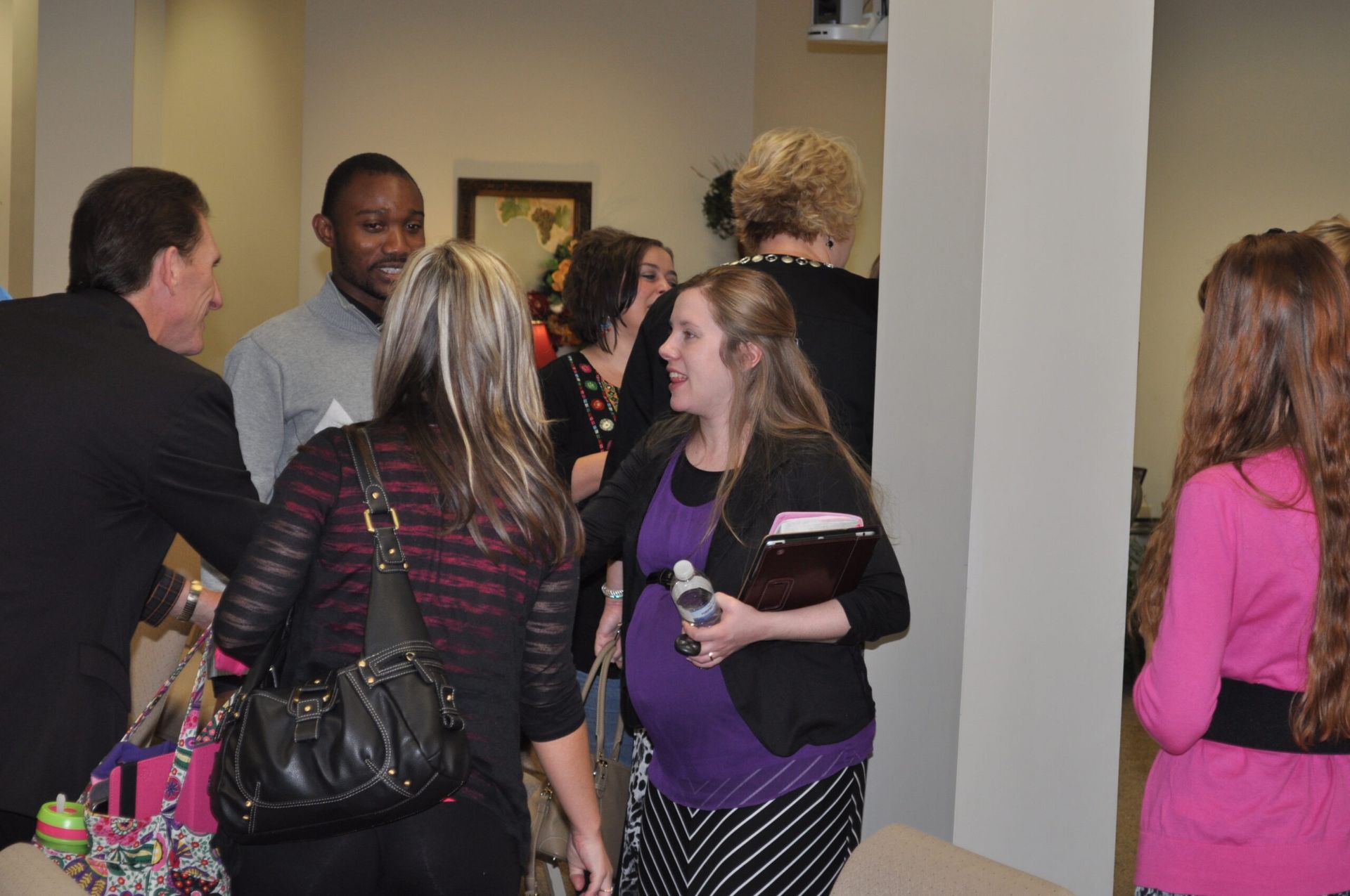 Group of people in an interior space; a pregnant woman smiles.