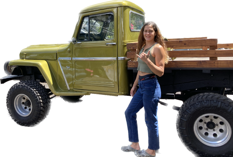 A woman is standing next to a green truck with a wooden bed.