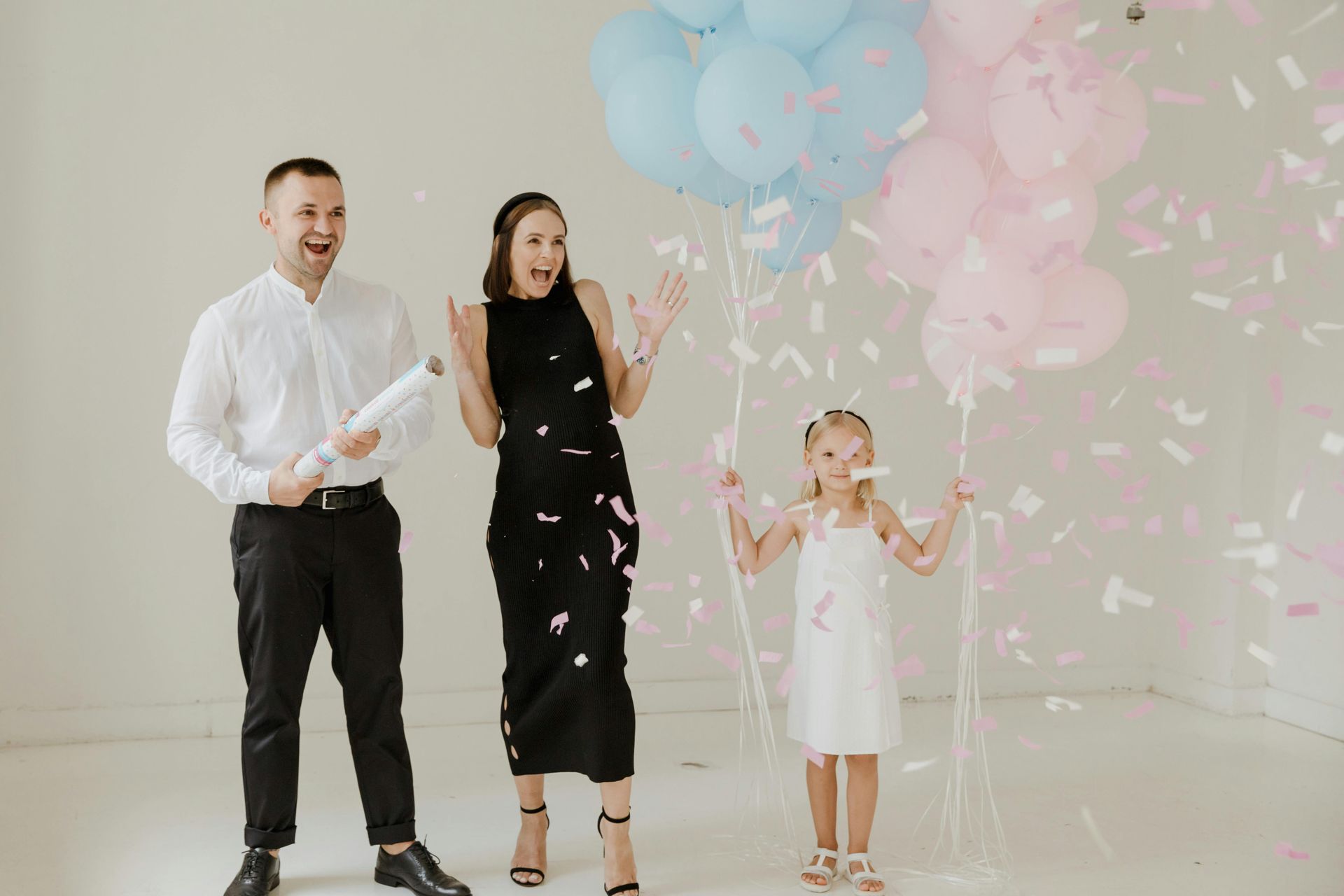 Familie viert geslachtsonthulling met confetti en ballonnen; moeder, vader en kind zijn opgewonden.