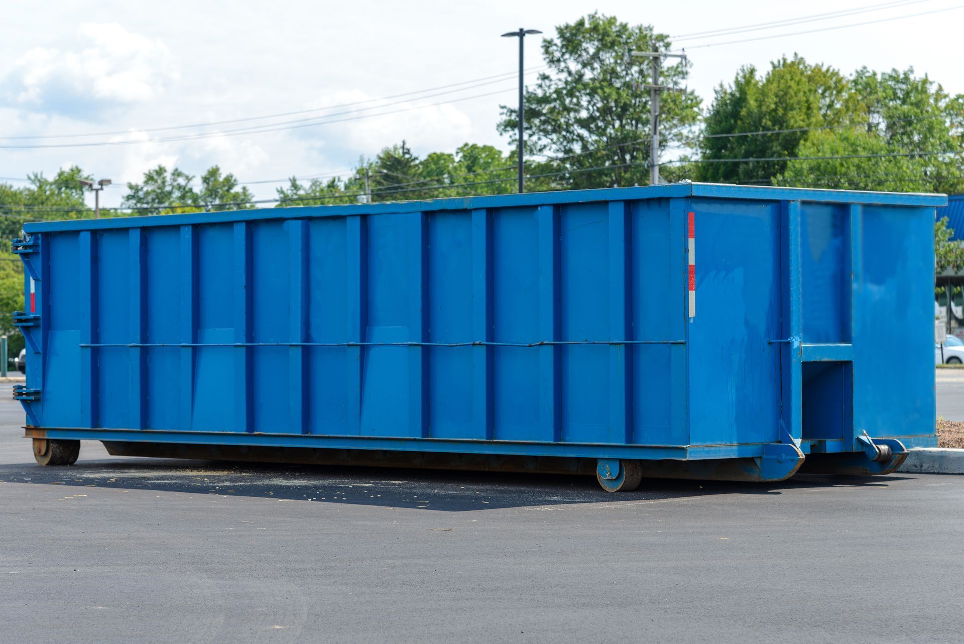 A large, blue, iron dumpster container is in the middle of a road, under the sun.