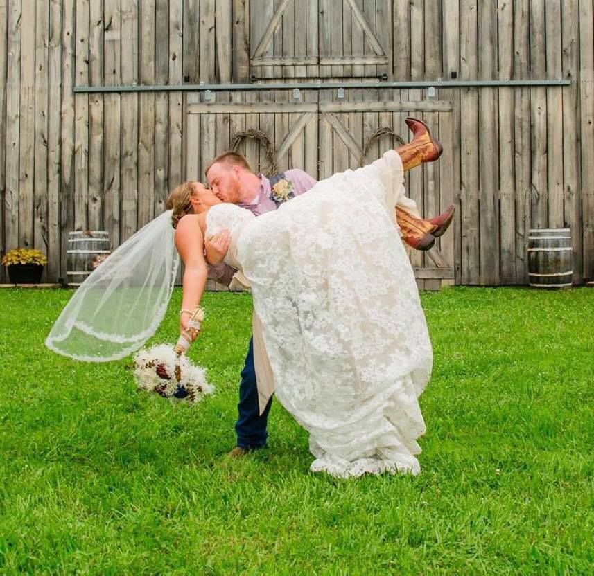 Wedding couple posing in a field, groom dipping bride in white gown and veil