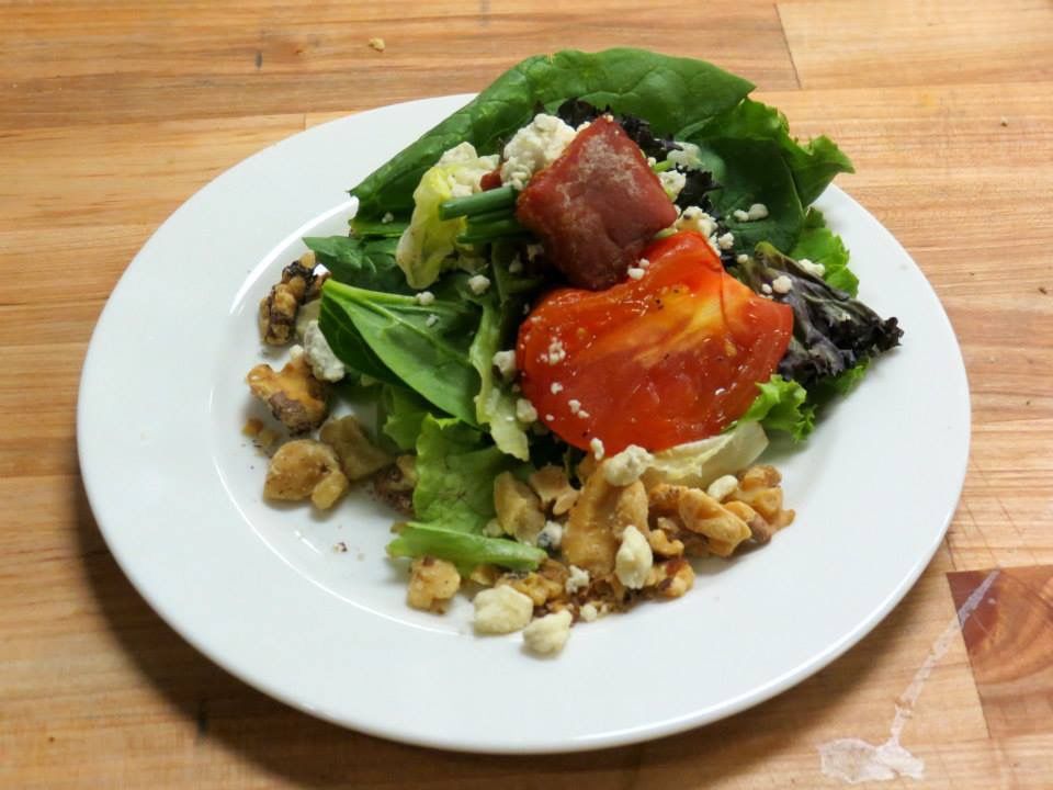 Mixed green salad with red tomatoes, walnuts, and croutons on a white plate