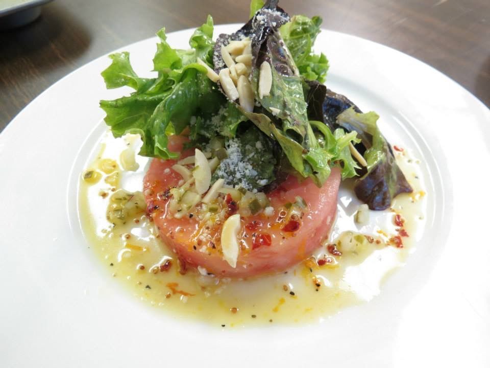 Tomato salad topped with greens and herbs, drizzled with dressing on a white plate