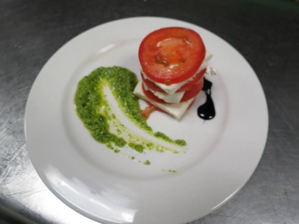 Plated tomato and mozzarella stack with basil sauce and balsamic drizzle on a white plate