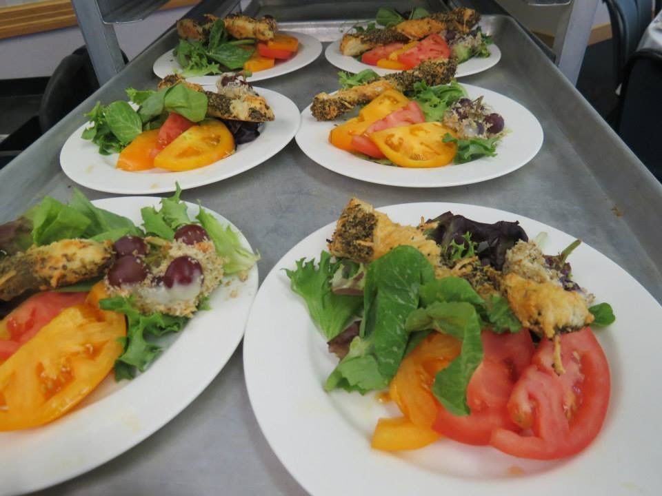 Plates of salad with tomato, greens, and roasted vegetables arranged on a metal tray