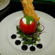 Gourmet red tomato appetizer with cream, greens, and crispy garnish on a white plate with sauce dots