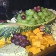 Fruit and cheese platter with green and red grapes, mango cubes, pineapple, and melon slices
