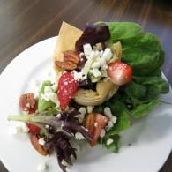 Side salad with mixed greens, strawberries, nuts, and crumbled cheese on a white plate