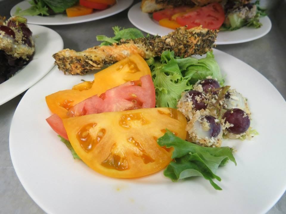 Plate with sliced tomatoes, greens, and a stuffed roll on a white dish, with more plates in the background