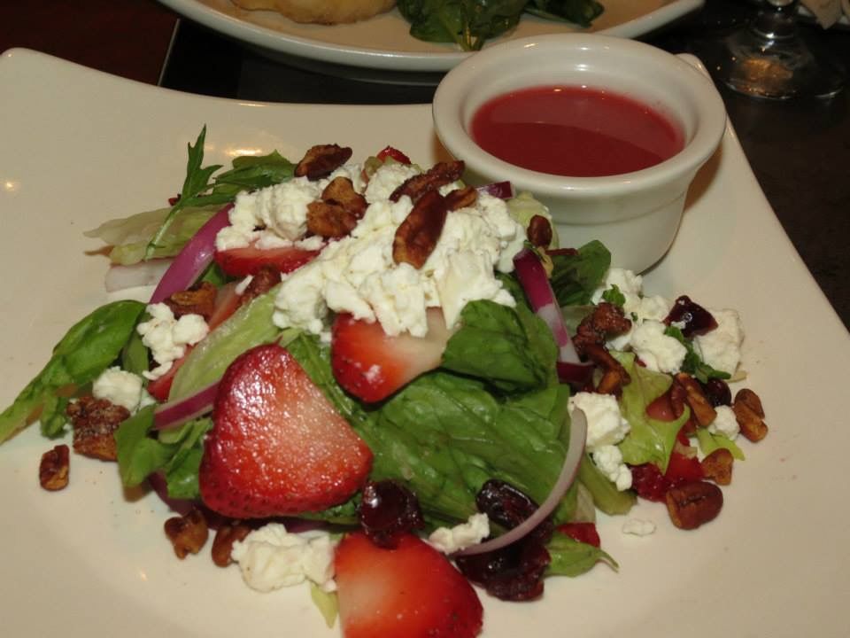Strawberry spinach salad with goat cheese and red dressing on a white plate