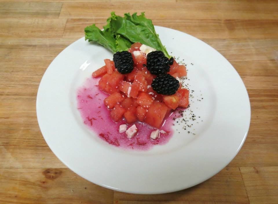 Dessert plate with pink cream, diced strawberries, blackberries, and mint on a white plate.