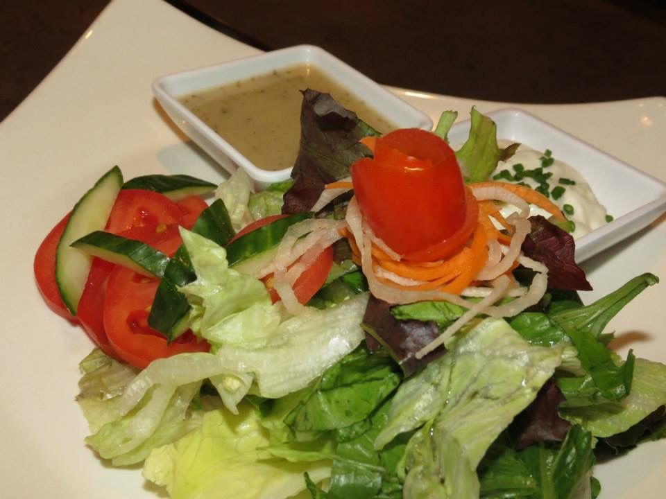 Mixed green salad with tomato, cucumber, and carrot garnish on a white plate