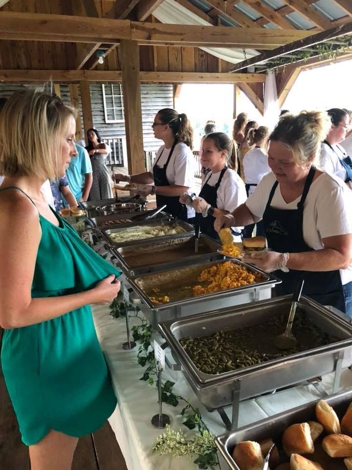 Buffet line at a wooden pavilion, with a woman in a green dress serving herself food.