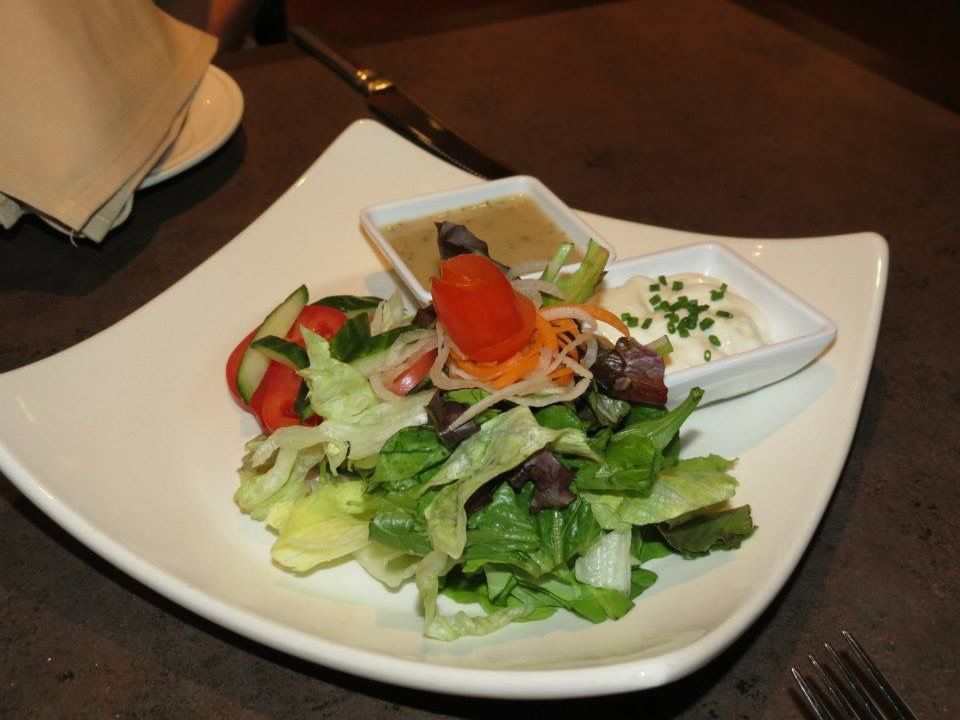 Salad on a white plate with mixed greens, tomatoes, and dressing on a dark table