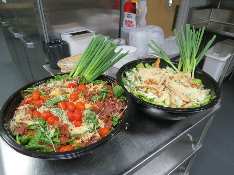 Two black bowls of prepared food topped with green onions on a stainless steel kitchen counter