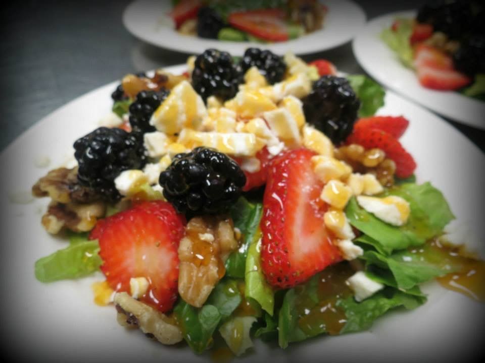 Fruit and nut salad topped with strawberries, blackberries, and chopped cheese on lettuce