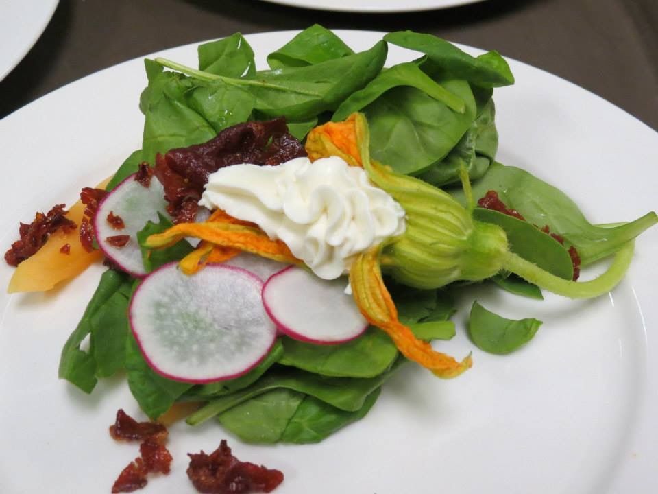 Mixed green salad with radish slices, carrot ribbons, and a dollop of dressing on a white plate