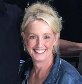 Smiling woman with blonde hair in a denim jacket against a dark background