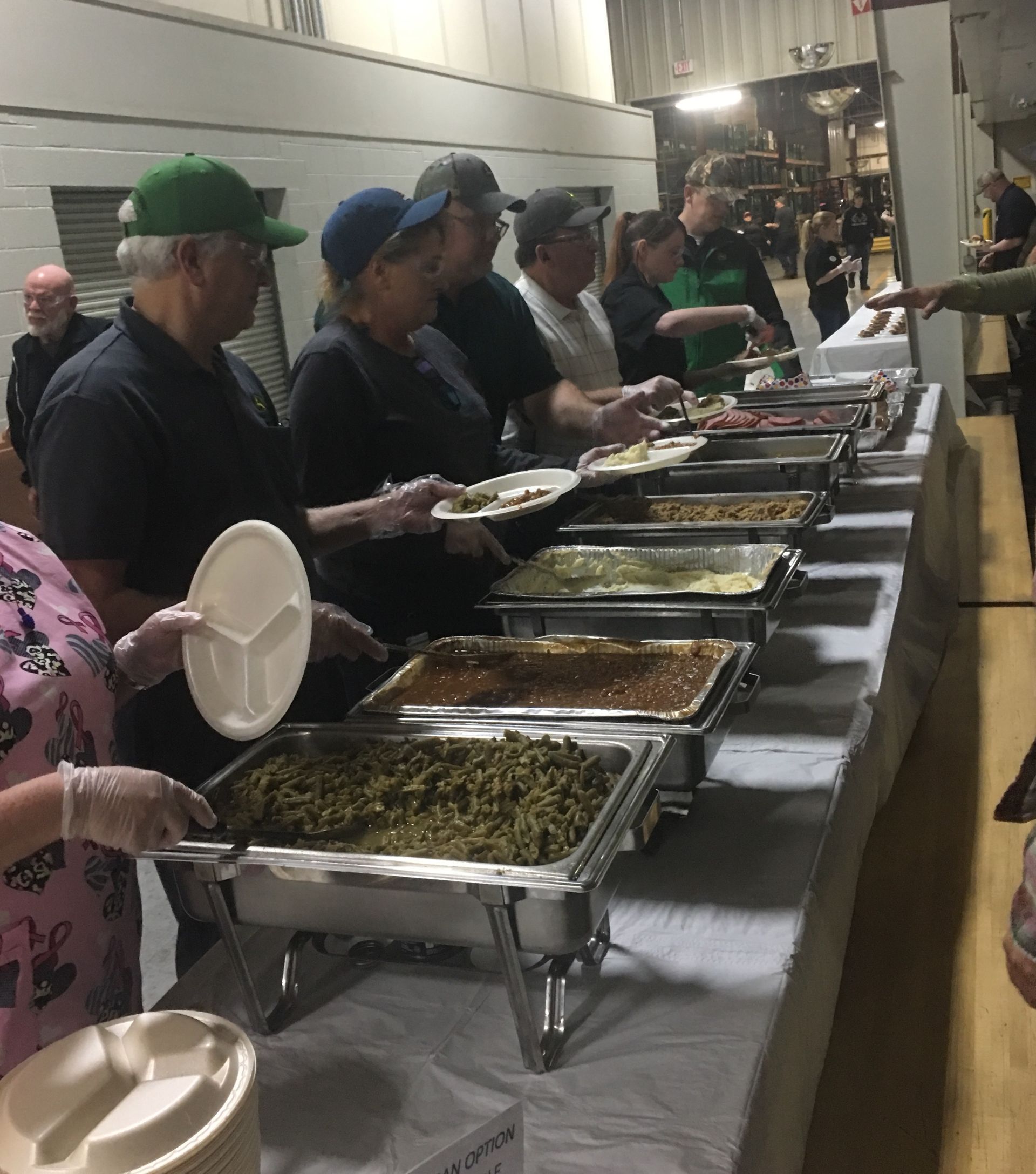People serving themselves from a long buffet line with trays of food in a hall