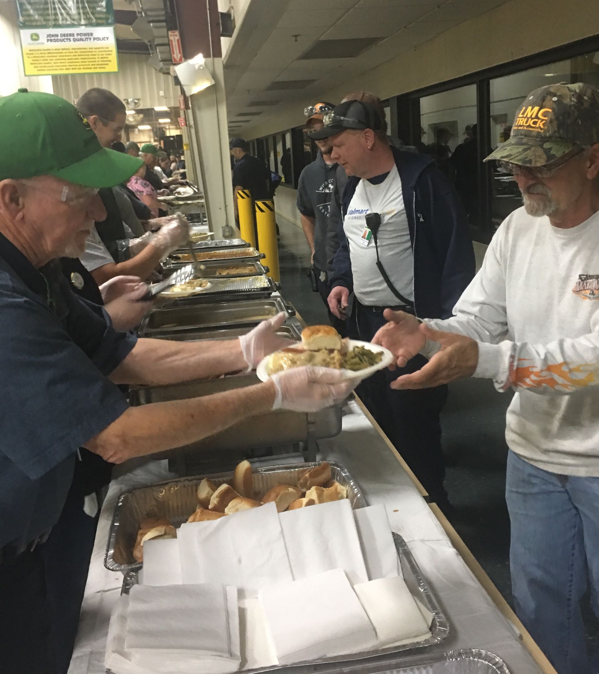 People serving food to attendees at a buffet counter in an indoor gathering hall.