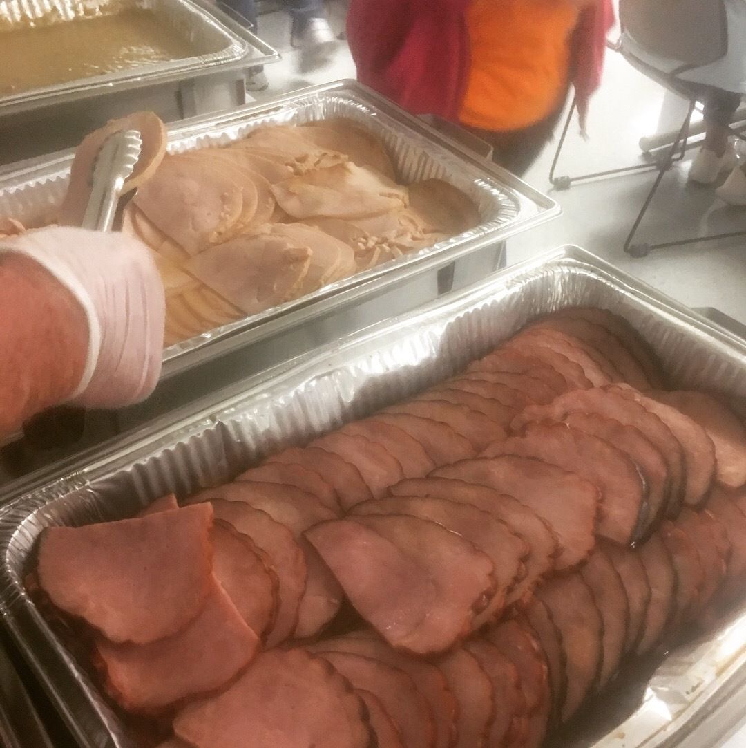 Tray of sliced roast meat at a buffet with a gloved hand serving from another pan