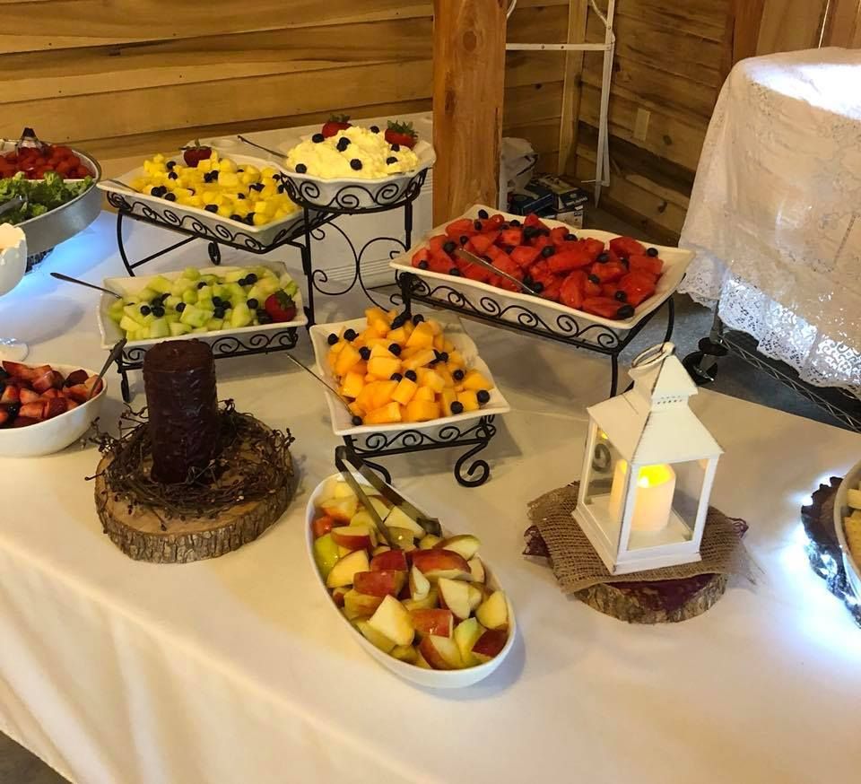 Buffet table with assorted fruit platters, dessert trays, and a lit lantern in a wooden room