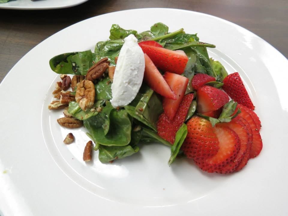 Spinach and strawberry salad with pecans and a dollop of goat cheese on a white plate