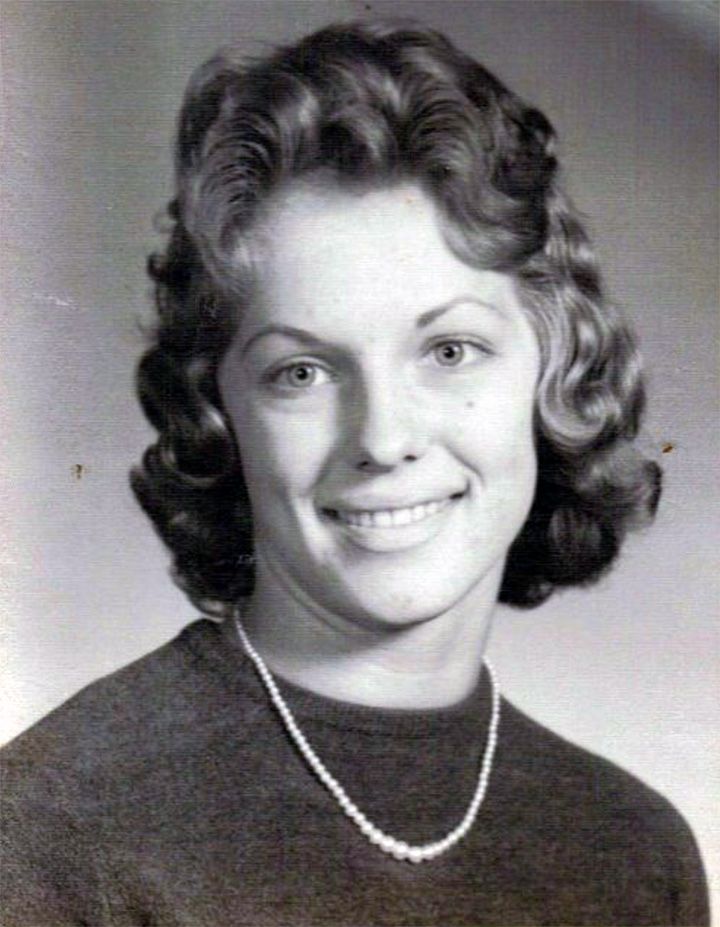 Black-and-white portrait of a smiling person in a dark top and necklace
