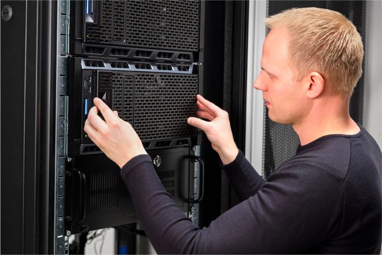 A technician installs a black server unit into a rack cabinet in a data center.