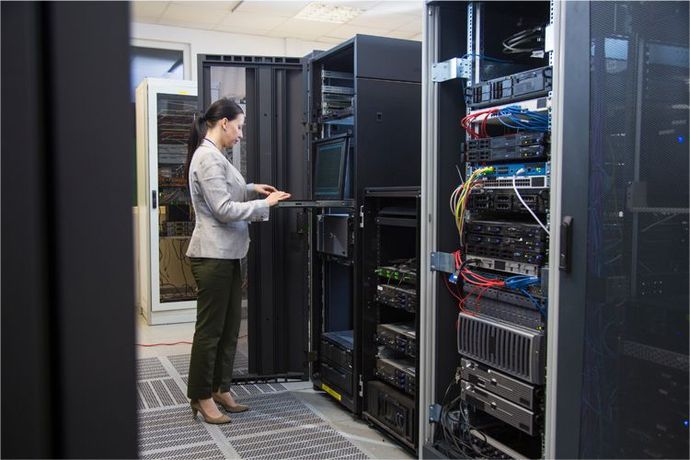 A person in business attire works on a rack-mounted server console inside a data center filled with network equipment.