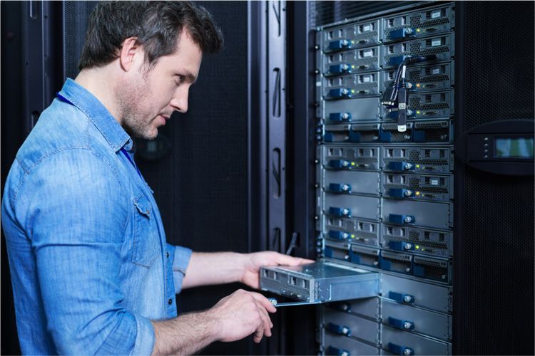 A person in a blue shirt installing or removing a server blade from a rack-mounted system in a data center.