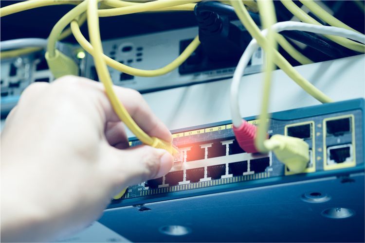 A person plugging a yellow Ethernet cable into a network switch in a server rack.