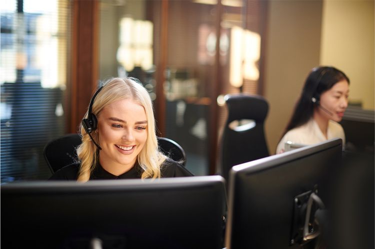 Two customer service representatives wearing headsets work at computers in a professional office setting.