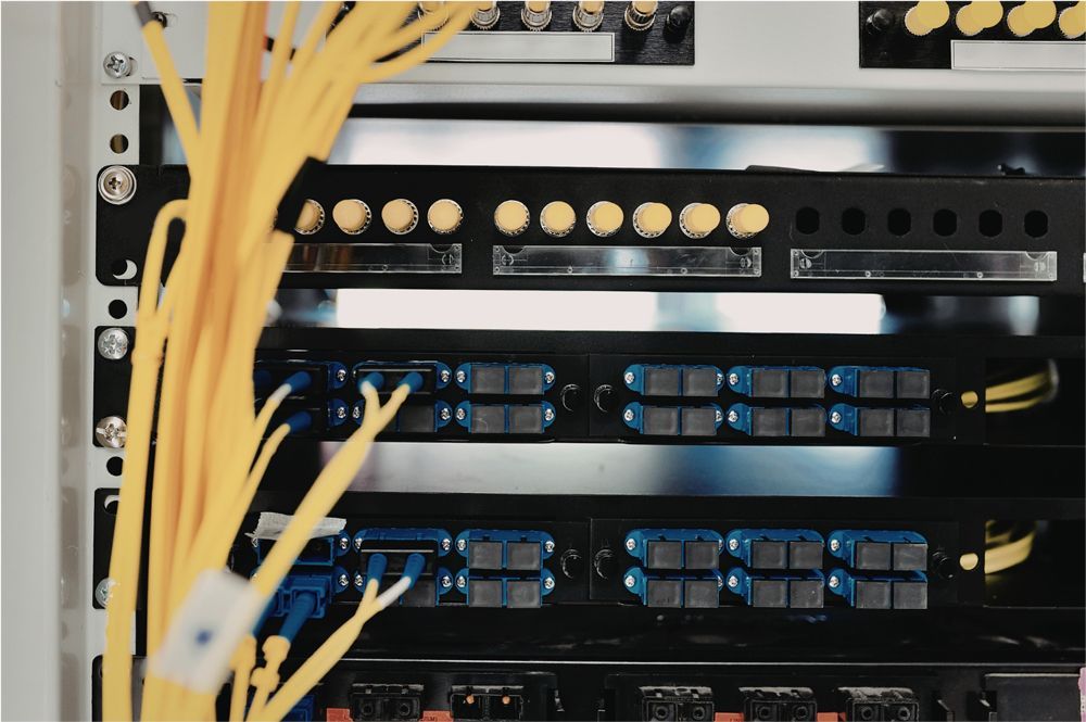 A server rack with rows of fiber optic patch panels connected by bright yellow cables.