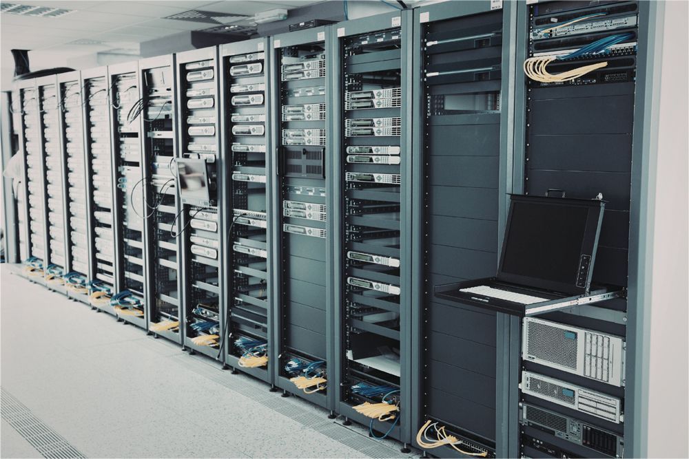 A row of server racks in a data center, with a laptop open on a shelf in the foreground.