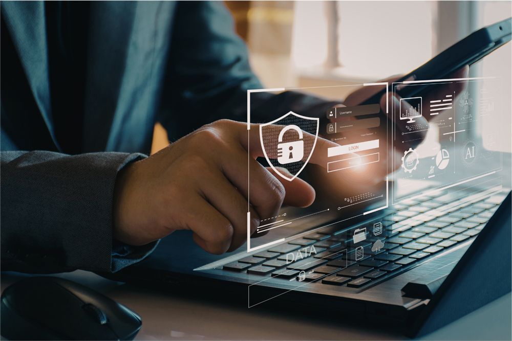 A person in a suit uses a smartphone over a laptop, with a digital overlay showing a shield and padlock icon for security.